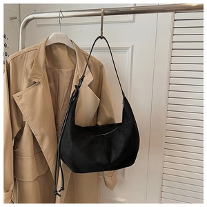 Detail of a black matte suede hobo bag hanging on a stylish beige coat rack setup