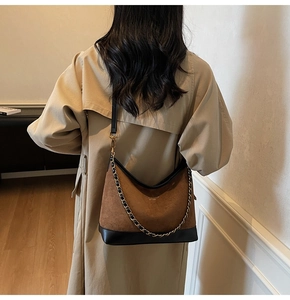 Detail of brown faux suede shoulder bag featuring a gold chain strap and black leather trim