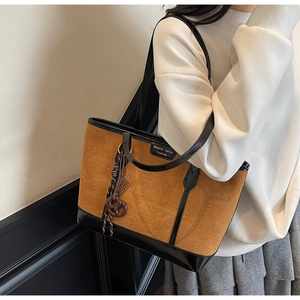 Detail of tan suede tote bag with black leather trim and decorative brand tag charm