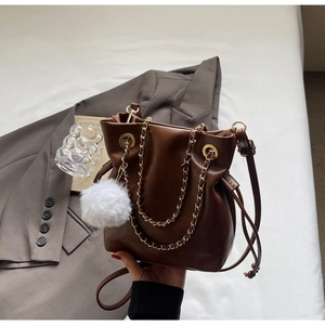 Detail of a brown leather drawstring bucket bag with gold chain and white fur pompom charm