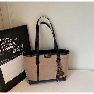 Close-up of beige tote bag with black leather trim and decorative woven pendant