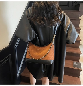 Detail of a brown suede and black leather patchwork saddle bag with golden chain detail