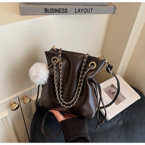 Detail of dark brown drawstring bucket bag featuring a white pom-pom and gold chain strap