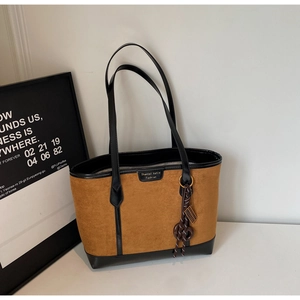 Detail of vintage caramel suede tote bag with golden nameplate and stylish braided ornament