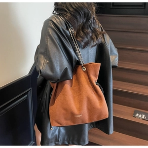 Détail d'un sac seau en daim marron avec bandoulière en chaîne dorée sur un escalier