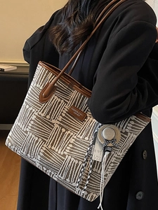 Fashionable brown striped woven tote bag with leather handles shown on shoulder