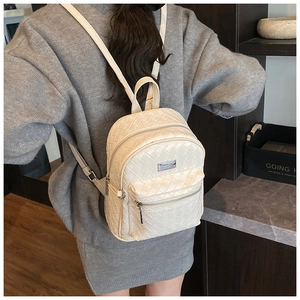 Détail du sac à dos tressé blanc sur un mannequin avec logo métallique et fermeture éclair