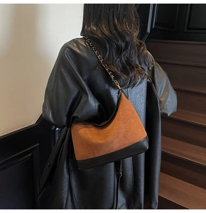 Detail of a brown suede and black leather patchwork underarm bag with a metal chain strap