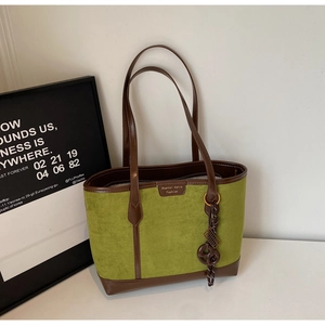 Detail view of green suede tote bag with brown leather handles and heart charm