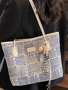Blue and white woven tote bag with beige leather trim and creative charms on a model