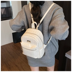 Détail d'un sac à dos blanc tressé avec poche zippée et plaque logo métallique sur le cuir
