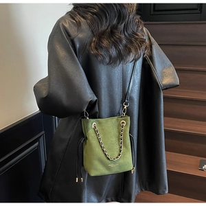 Détail du sac seau en daim vert herbe avec chaîne dorée et bandoulière en cuir noir chic