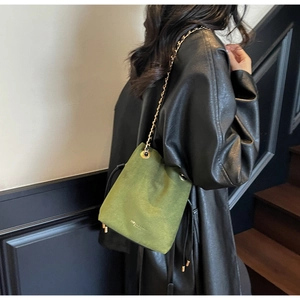 Détail du sac seau en daim vert avec œillets dorés et bandoulière chaîne sur un mannequin