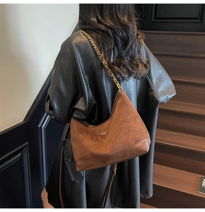 Close-up of brown suede hobo bag with gold chain strap worn by model in leather jacket