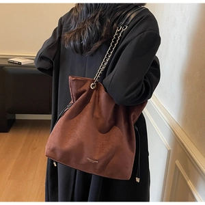Détail d'un sac seau marron en daim avec chaîne dorée et finition texturée élégante