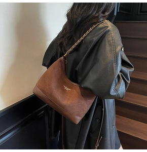Detail view of brown matte shoulder bag featuring gold chain strap and elegant brand logo