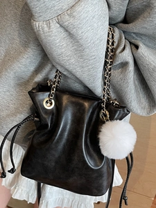 Fashionable black drawstring bucket bag with metal chain strap and white pompom pendant