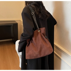 Détail du sac seau marron en aspect suède avec une élégante bandoulière en chaîne et cuir