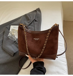 Detail of brown matte suede shoulder bag with retro gold chain and brand logo lettering