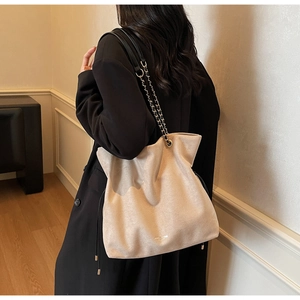 Détail du sac seau en daim beige avec bandoulière en cuir noir et chaîne dorée