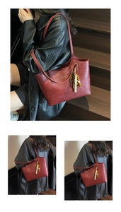 Detail of burgundy faux leather tote bag with gold logo and wooden bead tassel decoration