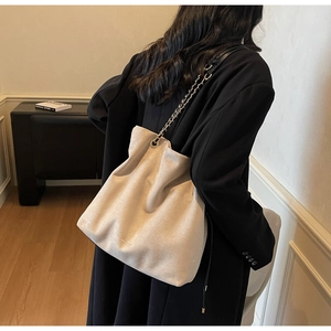 Détail du sac seau en daim beige avec logo doré et bandoulière en chaîne métal