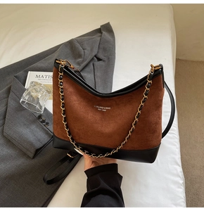 Detail of a contrast suede and leather Boston bag with chain strap on a white surface