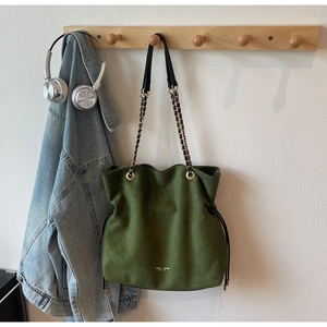 Détail du sac seau en daim vert avec bandoulière chaîne dorée et fermeture à cordon