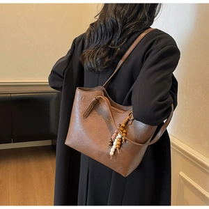 Detail of a dark brown vintage leather tote bag with unique beaded ethnic style charm