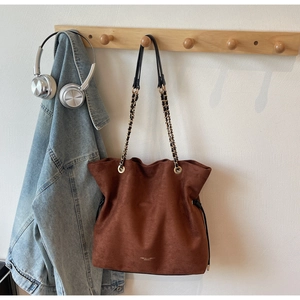 Détail du sac seau en daim marron avec logo doré et bandoulière en chaîne métal