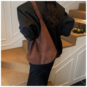 Brown suede tote bag shown on a model's shoulder against a vintage interior
