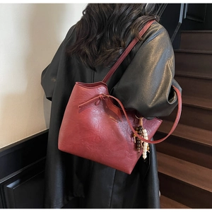 Detail of burgundy pebbled leather tote bag with beaded charm and decorative bow accent