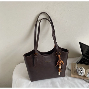 Detail of dark coffee tote bag with gold logo, metal buckle and colorful wood bead tassel