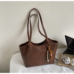 Detail of vintage brown tote bag featuring embossed logo and colorful beaded pendant charm