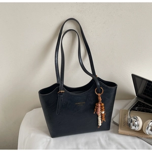 Detailed view of black tote bag with gold logo on desk with laptop and books