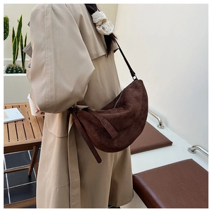 Detailansicht einer braunen Wildleder-Halbmondtasche an einem Model in einem Café
