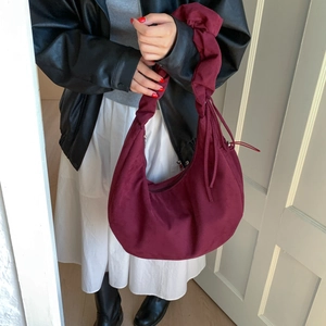 Detail of burgundy velvet croissant bag featuring pleated handle and drawstring design