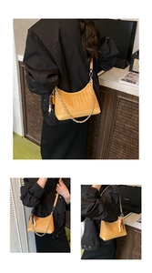 Detail of ginger woven saddle bag with leather strap, metal chain, and wooden bead pendant