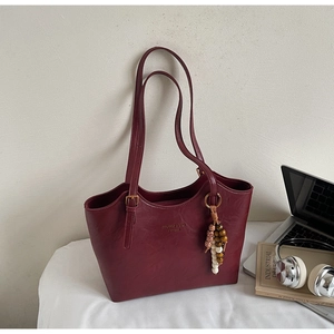 Detail of burgundy leather tote bag with long straps and stylish beaded tassel charm