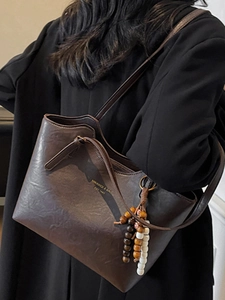 Retro brown leather tote bag with wooden bead charm worn by a model in black coat