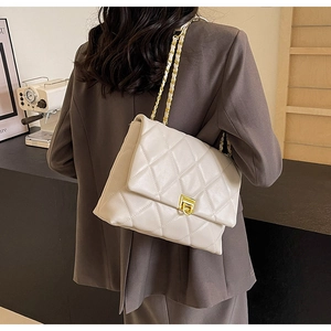 Detail of a beige quilted chain bag featuring a gold metal twist lock and leather strap