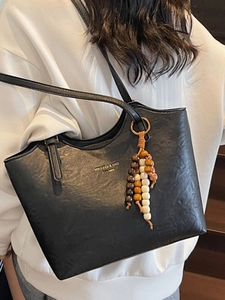 Black leather tote bag with gold logo and beaded charm, shown worn on shoulder