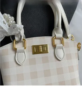 Detailed macro view of beige checkered handbag featuring gold hardware and pearl lace charm