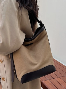 Minimalist khaki canvas tote bag with black leather trim worn on shoulder by a model