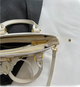Detail of cream leather handbag showing smooth gold zipper and pearl charm attachment
