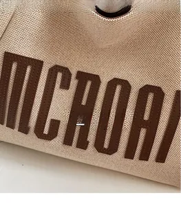 Détail du sac cabas en toile beige avec broderie de lettres en cuir brun et couture fine