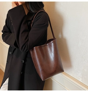 Détail d'un grand sac cabas en cuir ciré marron foncé porté avec un blazer noir