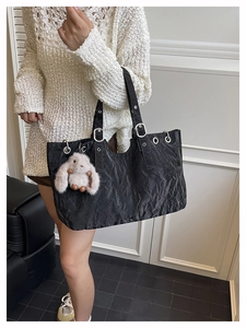 Détail du sac cabas noir en tissu plissé avec œillets argentés et pendentif lapin en peluche