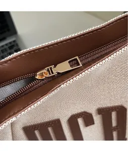 Détail d'un sac cabas en toile avec garniture en cuir brun et fermeture éclair dorée