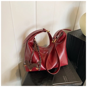 Detail of burgundy leather bucket bag with brown puppy pendant and gold metal buckle